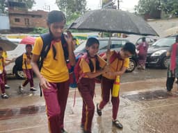 सुबह हुई बारिश के दौरान स्कूल जाते बच्चे