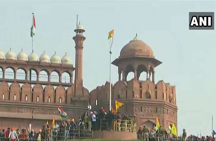 A protestor hoists a flag from the ramparts of the Red Fort in Delhi लाल किले पर किसानों ने फहराया झंडा, दिल्ली पुलिस के सामने किया शक्ति प्रदर्शन